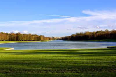 River and grassy field against cloudy sky on sunny day