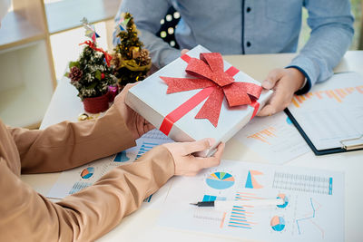 Midsection of business colleagues with christmas present over documents at office