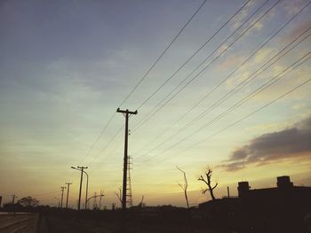 Power lines against sky at sunset