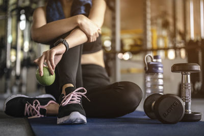 Low section of woman sitting on exercise mat in gym