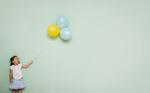 Girl  holding a bunch of colorful balloons against a blank teal wall 