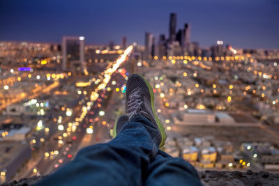 Low section of man with illuminated cityscape against sky at night