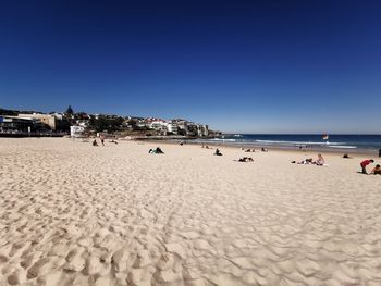 Group of people on beach against clear blue sky