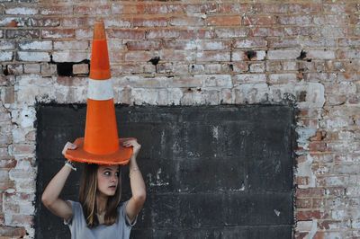 Woman holding traffic cone on head while standing against wall