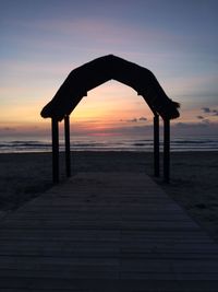 Silhouette pier on beach against sky during sunset