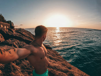Shirtless man swimming in sea against sky during sunset