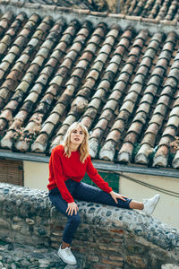 Portrait of young woman sitting on railing against roof tiles