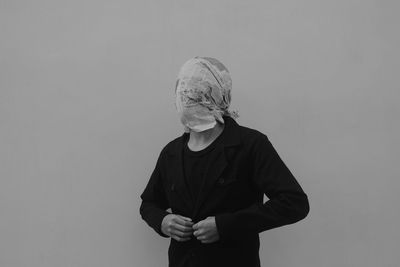 Man with face covered in newspaper standing against gray wall