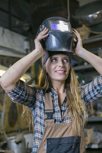 Smiling woman wearing helmet while standing in factory