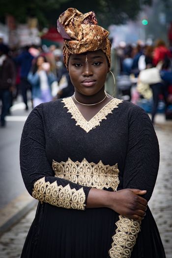 CLOSE-UP PORTRAIT OF YOUNG WOMAN STANDING AGAINST BLURRED BACKGROUND