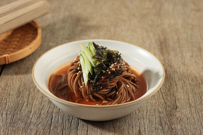 Close up korean cold soba noodle bibim guksu with cucumber, nori flakes, and sesame seed