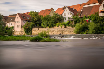 Flowing water with houses and trees against sky