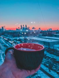 Close-up of hand holding cup against sky during sunset