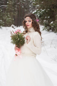 Beautiful bride in a white dress with a bouquet in a snow-covered winter forest. 