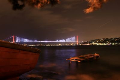 Illuminated bridge over river against sky at night