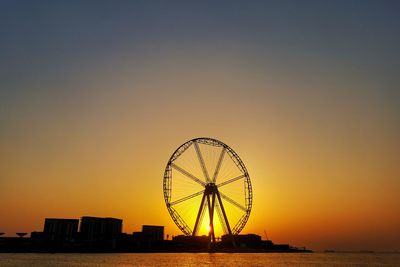 Silhouette ferris wheel by sea against romantic sky at sunset