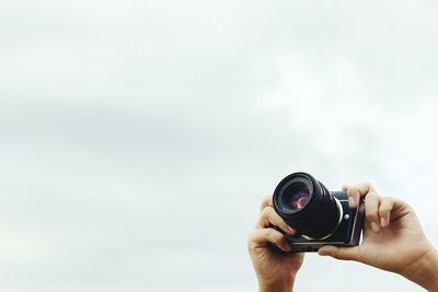 Low angle view of person photographing with digital camera against sky