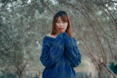 Portrait of a beautiful young woman standing against trees