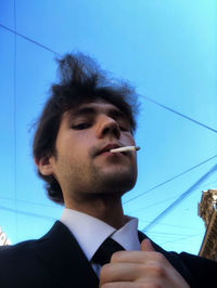 Portrait of young man looking away against blue sky