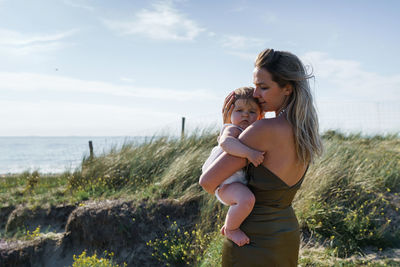 Full length portrait if woman with child standing on land against sky