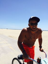 Young man wearing sunglasses on beach against clear sky