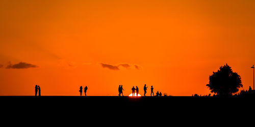 Silhouette people against orange sky