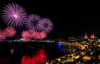 Firework display over illuminated city against sky at night