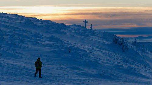 People skiing on snowcapped mountain against sky during sunset