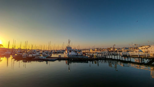 Sailboats moored in harbor at sunset