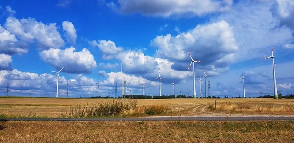 Panoramic view of wind turbines on field against sky