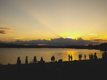 Silhouette people standing by sea against sky during sunset