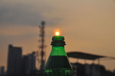 Close-up of illuminated bottle against building during sunset