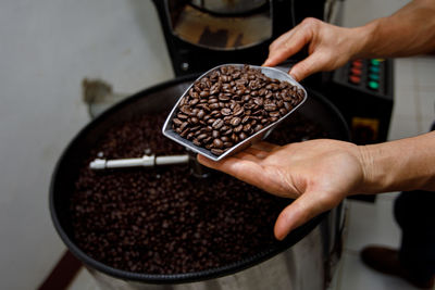 Close up hand holding a probe of fresh roasted coffee beans and spinning machine background