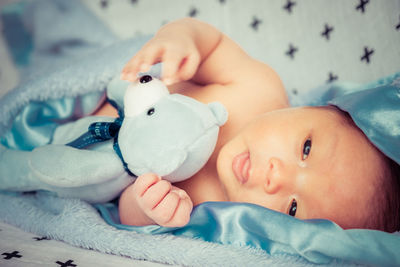 Close-up of shirtless baby with stuffed toy lying on bed