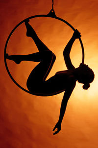 Silhouette woman with arms raised against sky during sunset