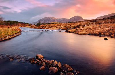 Sunrise scenery, river and mountains under dramatic orange sky, derryclare, galway, ireland