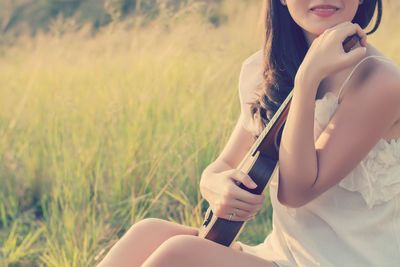 Midsection of woman playing violin while sitting on field