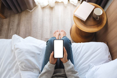 Low section of woman using mobile phone on bed at home