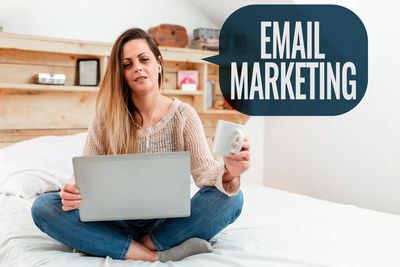 Young woman using mobile phone while sitting on bed