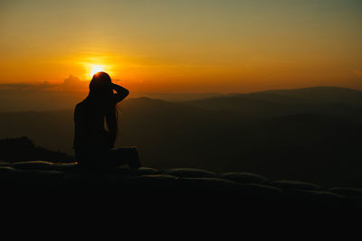 Silhouette man standing on rock against sky during sunset