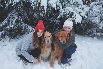 Portrait of female friends with golden retrievers on snow covered field