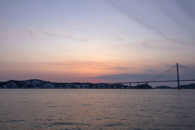 Suspension bridge over sea against sky during sunset