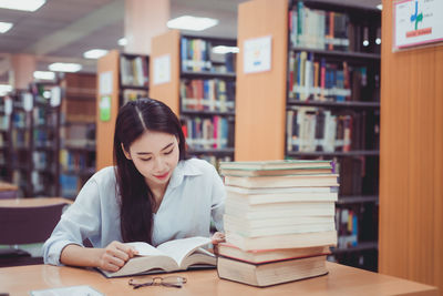 Beautiful young woman reading book in library