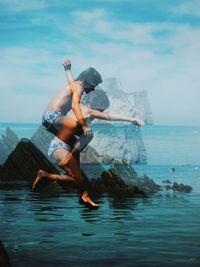 Full length of shirtless man in sea against sky