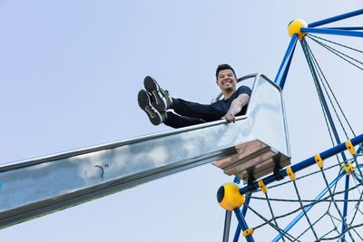 Low angle view of man sitting on slide against blue sky