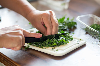 Close-up of cropped hands cutting leaf vegetables on cutting board in kitchen