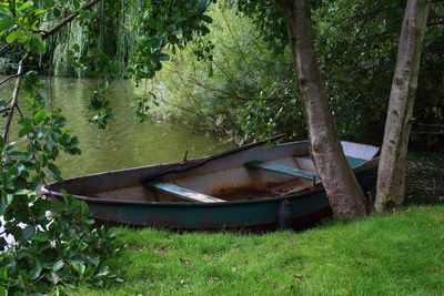 Abandoned boat moored on grass by lake