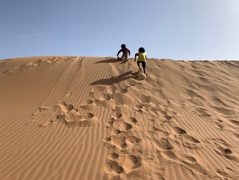 Kids walking on sand dune in desert against sky