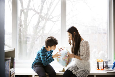 Mother and son looking at globe against window at home