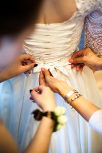 Close-up of woman assisting bride for getting dressed